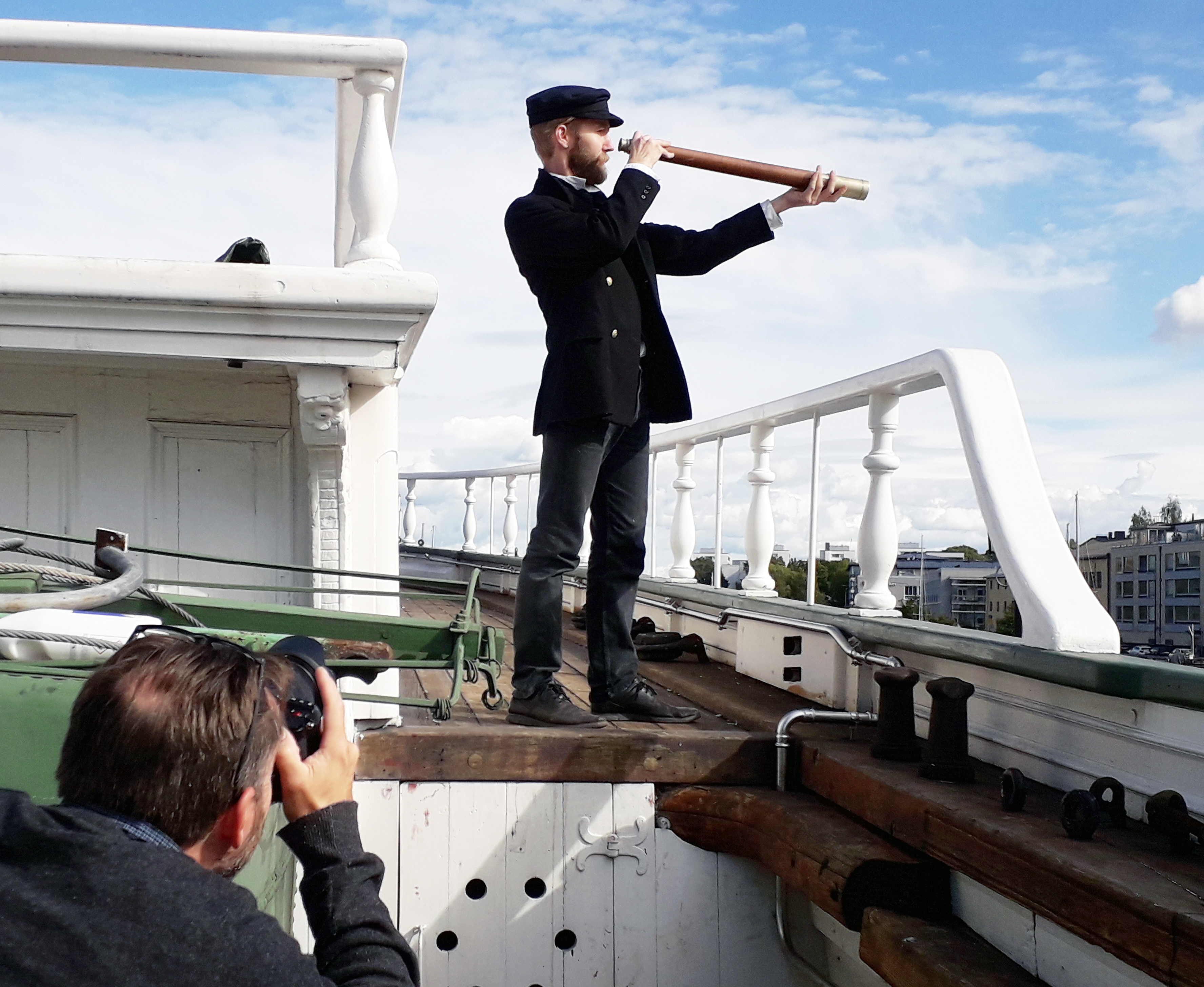 Kaptenen spanar ut mot horisonten – fast i det här fallet närmast in mot staden. Timjami Varamäki greppar tubkikaren uppe på däck, medan Anders Wik hanterar det modernare optiska instrumentet, dvs. systemkameran.